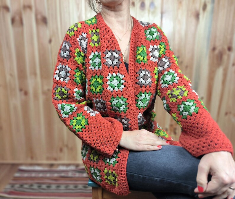 May include: A red, green, and brown crocheted cardigan with a granny square pattern. The cardigan is open in the front and has long sleeves.