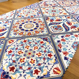 Peut inclure: Un chemin de table avec un motif géométrique composé de couleurs bleues, rouges, jaunes et blanches. Le motif rappelle les motifs traditionnels des carreaux.