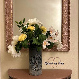 May include: A white and yellow flower arrangement in a gray, decorative vase with a mandala design. The vase is sitting on a half-round table with a rose gold finish. The text "Upcycle by Amy" is visible in the lower right corner of the image.