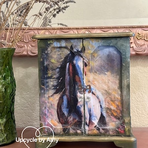 May include: A small wooden cabinet with two doors, painted in a green and gold color scheme. The doors feature a colorful painting of a horse running through a field. The cabinet has a decorative gold trim and sits on a wooden surface. The text "Upcycle by Amy" is visible in the lower left corner of the image.