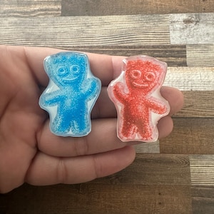 May include: Two gummy candy figures, one blue and one red, with a textured surface. The figures are shaped like people with arms raised and smiling faces.