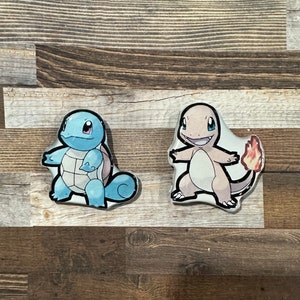 May include: Two cartoon Pokemon characters, Squirtle and Charmander, are depicted in a blue and orange color scheme. The characters are standing on a wooden surface.