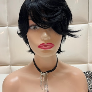 May include: A mannequin head with a short, black wig and a black choker necklace with dangling rhinestones and iridescent teardrop-shaped pendants. The mannequin has full red lips and is set against a white background.