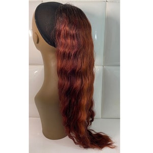 May include: A long, wavy, auburn-colored hair extension with a black elastic band. The hair extension is attached to a mannequin head.