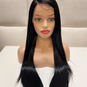 May include: A black, long, straight wig on a mannequin head. The wig has a side part and is styled with a natural hairline. The mannequin has red lipstick and is set against a white background.