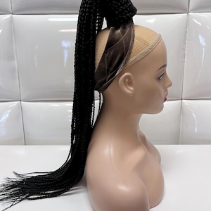 May include: A black braided ponytail hair extension with a brown velvet headband. The hair extension is attached to a mannequin head.