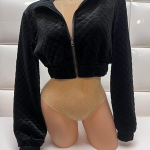 May include: A black quilted cropped jacket with a zipper closure. The jacket has a high collar and long sleeves.