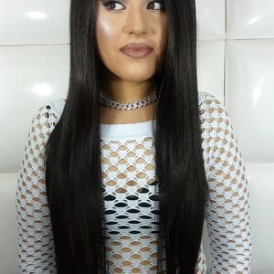 May include: A woman with long, straight black hair wearing a white mesh top and a silver chain necklace.