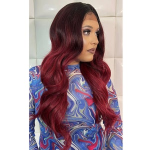 May include: A long, wavy, dark red and black ombre wig with a lace front. The wig is styled in loose waves and falls to the shoulders.