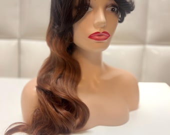 May include: A mannequin head with a two-toned wig. The wig features dark brown roots that transition to a reddish-brown ombre. The hair is styled with side-swept bangs and long, wavy layers. The mannequin has red lipstick.