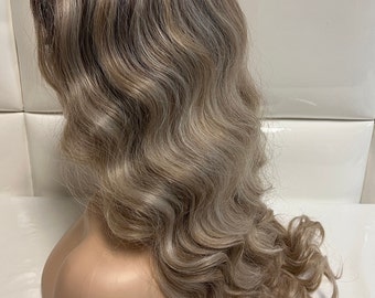 May include: A long, wavy, light brown wig with blonde highlights. The wig is styled in loose waves and has a natural-looking parting.