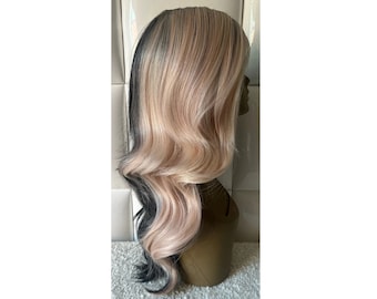 May include: A long, wavy wig with a side part, featuring a blend of light blonde and black strands. The wig is styled with voluminous curls and is displayed on a mannequin head, showcasing its layered design and color variations.