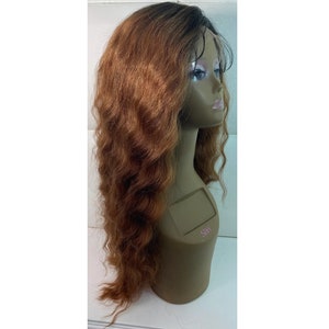 May include: A long, wavy wig with a blend of brown and auburn tones, styled on a mannequin head. The wig features a dark root and a lace front for a natural look. The hair cascades down the mannequin's shoulders.