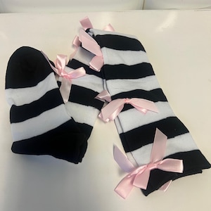May include: A pair of black and white striped socks with pink bows. The socks are knee-high and feature horizontal stripes. The bows are tied at the top of the socks.