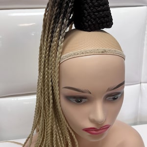 May include: A long blonde and brown ombre braided ponytail hair extension. The hair is attached to a brown mesh hairpiece.