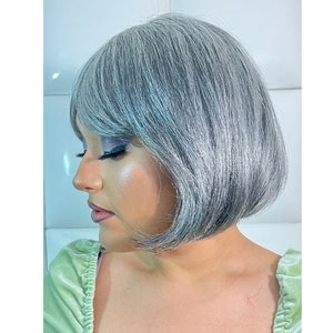 May include: A silver bob wig with a side part and bangs. The wig is styled in a straight, blunt cut.