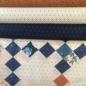 May include: A stack of fabric featuring various patterns in shades of blue, white, and orange. The fabric is rolled up and has a white background with blue and orange geometric shapes.