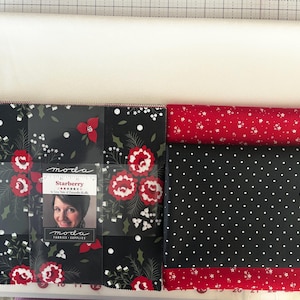 May include: A collection of fabric squares and rolls. The fabric squares feature a black background with red floral and white accents. Rolls of fabric include a red and white star pattern and a black and white polka dot pattern. The label reads "Starberry".