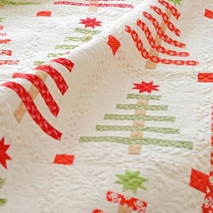 May include: A white quilt with a repeating Christmas tree pattern. The trees are made of red and green fabric strips, with star and square accents. The quilt has a textured, quilted surface.