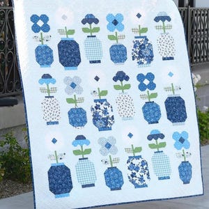May include: A rectangular quilt featuring a repeating pattern of various blue and white floral arrangements in vases. The design includes diverse shades of blue, light blue, and white fabrics with floral, plaid, and solid geometric patterns.