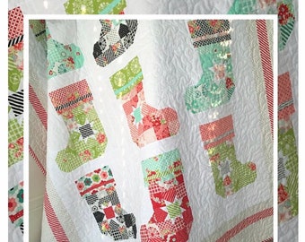 May include: A Christmas-themed quilt featuring patchwork stockings in various patterns and colors, including red, green, and black, set against a white background. The quilt has a quilted texture and is bordered with red and white stripes. The text "Ready for Santa" is visible.