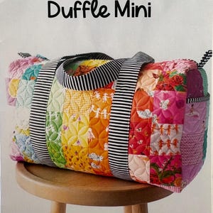 May include: A colorful patchwork duffle mini bag with a striped handle and accents. The bag features a variety of patterned fabrics in a rainbow of colors, including floral and geometric designs. The text "Patchwork Duffle Mini" is at the top.