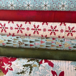 May include: Assortment of Christmas-themed fabric rolls. The fabrics feature various patterns, including snowflakes, Christmas trees, and floral designs. Colors include red, white, green, and blue. The fabrics are arranged on a green cutting mat.