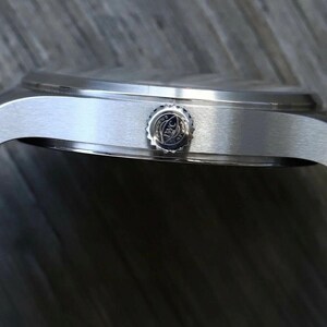 Puede incluir: Una vista lateral de una caja de reloj de acero inoxidable en tono plateado con acabado cepillado. El reloj presenta una corona circular grabada con el logotipo de IWC y est&aacute; sujeto a una correa de caucho negra con costuras blancas visibles.