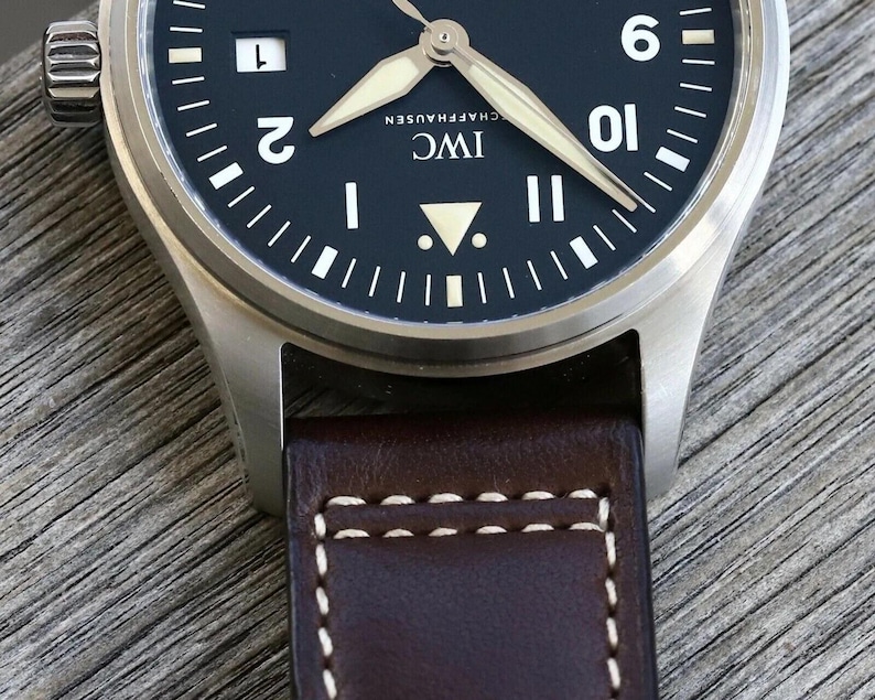 Puede incluir: Un reloj de pulsera de acero inoxidable con esfera negra mate, que presenta n&uacute;meros ar&aacute;bigos blancos en las posiciones de las dos, nueve y diez, una ventana de fecha, manecillas luminosas y una correa de cuero marr&oacute;n con costuras blancas.