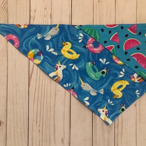 Può includere: Un bandana reversibile per cani blu e turchese con un tema di festa in piscina estiva da un lato e fette di anguria dall'altro.