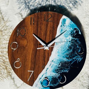 May include: A round wooden clock with a blue and white resin wave design. The clock face has Roman numerals and white hands.