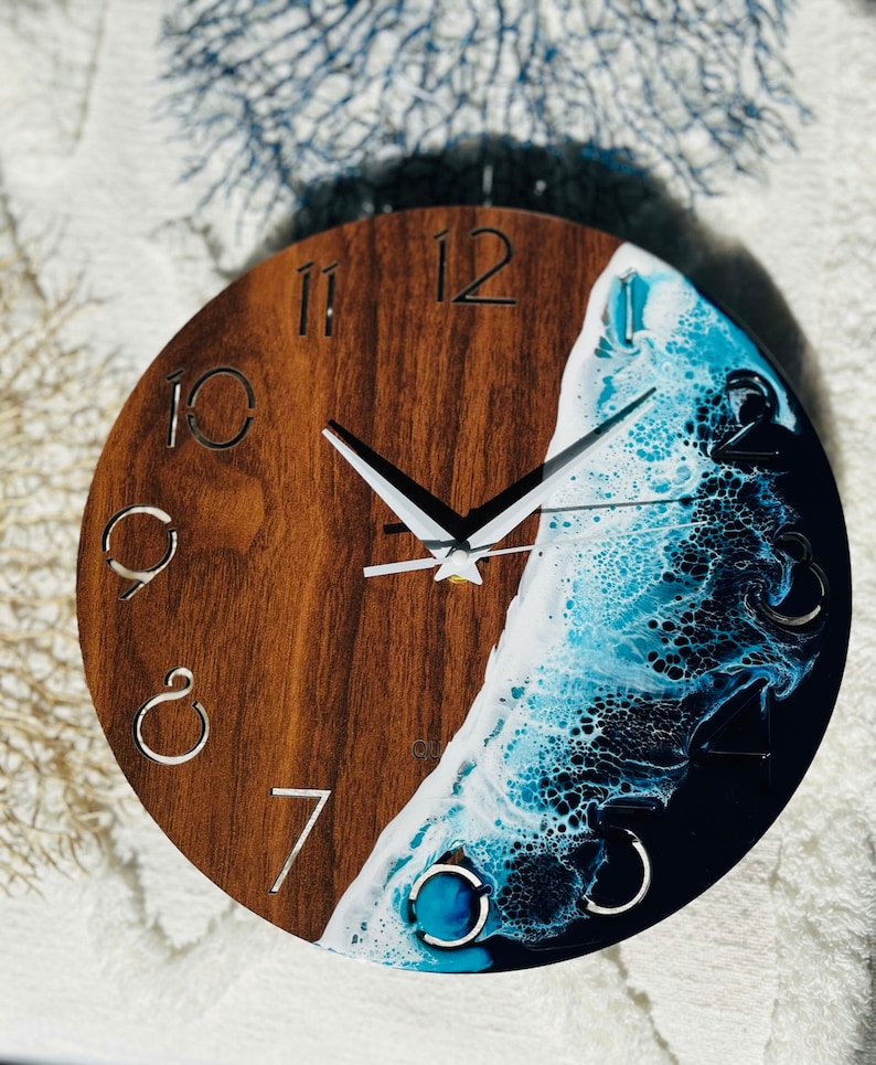 May include: A round wooden clock with a blue and white resin wave design. The clock face has Roman numerals and white hands.