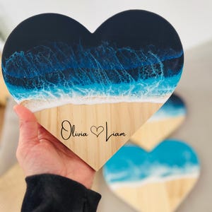 May include: A wooden heart-shaped plaque with a blue and white resin ocean scene. The plaque is personalized with the names "Olivia" and "Liam" and a heart symbol.