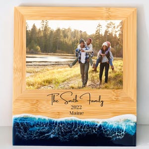 May include: A wooden photo frame with a blue and white ocean wave design at the bottom. The frame has a photo of a family of four in a field. The text "The Smith Family 2022 Maine" is inscribed on the frame.