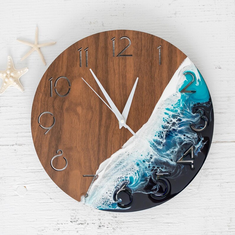 May include: A wooden clock with a blue, white, and black resin wave design. The clock face has Roman numerals and white hands.