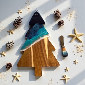 May include: A wooden Christmas tree-shaped serving board with a resin ocean design. The board is surrounded by starfish, pinecones, and a matching spreader. The resin art features shades of blue, white, and brown.