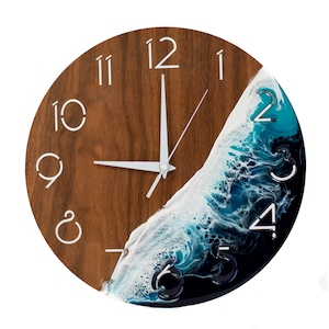 May include: A round wooden clock with white Roman numeral hour markers and white hands. The clock face is partially covered by a blue, white, and black resin wave design.