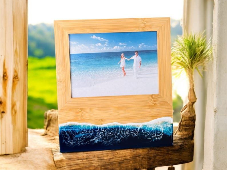 May include: A wooden picture frame with a blue and white resin base that resembles ocean waves. The frame holds a photo of a couple walking on a beach.