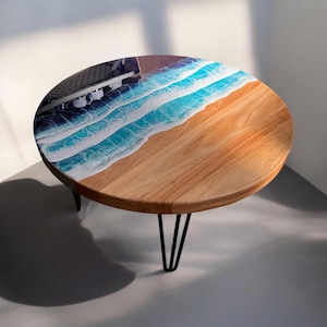 May include: Round wooden coffee table with black hairpin legs. The tabletop features a blue and white resin ocean wave design.