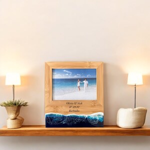 May include: A wooden photo frame with a beach scene and a couple walking on the sand. The frame is personalized with the text "Olivia & Nick 07.09.22 Barbados".