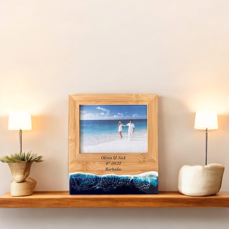 May include: A wooden photo frame with a beach scene and a couple walking on the sand. The frame is personalized with the text "Olivia & Nick 07.09.22 Barbados".