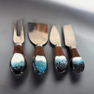 May include: Set of four cheese knives with wooden handles and blue and white resin accents. The knives have different blade shapes for various types of cheese.