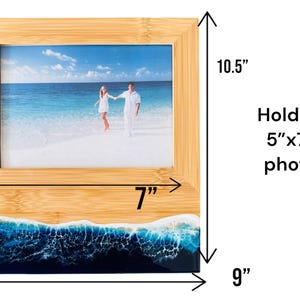 May include: A bamboo picture frame with a blue and white resin ocean wave base. The frame holds a 5" x 7" photo and measures 7" wide by 9" tall and 10.5" high.