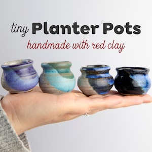 May include: Four small, handmade planter pots made with red clay. The pots are in various shades of blue, purple, and gray.