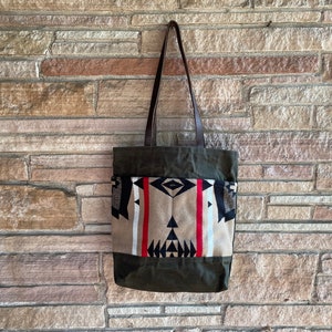 May include: A green canvas tote bag with leather straps and a patterned fabric insert. The fabric insert features a geometric design in black, white, red, and beige.