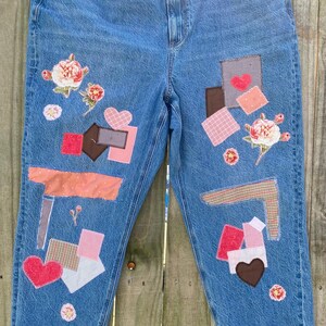 May include: Light blue denim jeans with decorative patches in various colors and patterns. Patches include hearts, floral designs, and geometric shapes. The jeans have a relaxed fit and are distressed.