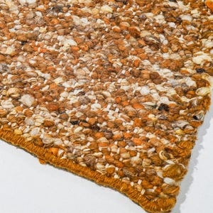 Pode incluir: Uma base para copos quadrada e texturizada com um padrão de mosaico de elementos bege, castanhos e brancos. A base para copos tem uma borda costurada laranja. O produto é da India Living.