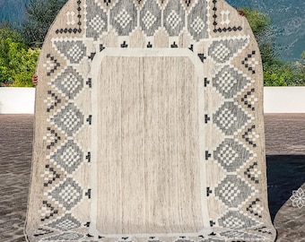 Pode incluir: Um tapete grande de cor branco-queimado com um padrão geométrico em tons de cinza e marrom. O tapete tem uma forma arredondada e está colocado em um pátio de pedra.