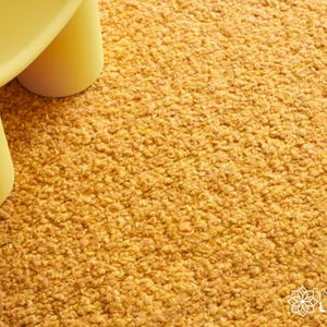 May include: A close-up of a yellow, rounded table with three legs on a textured, golden-yellow carpet. The carpet has a dense, looped pile. The table is a solid, matte color, and the carpet has a warm, inviting appearance.