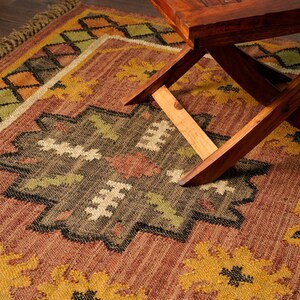 May include: A brown and yellow patterned rug with a wooden folding table on top. The rug has a geometric design with black, green, and white accents.